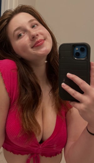 Woman in pink top taking mirror selfie indoors, smiling softly.