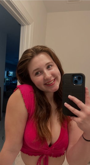 Woman in pink top taking mirror selfie indoors, smiling.