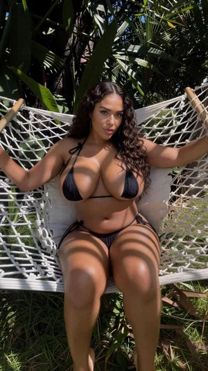 Woman in black bikini sitting in white hammock outdoors, surrounded by greenery.