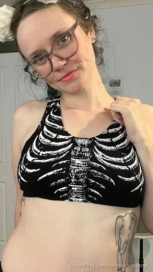 Woman with glasses and curly hair wears a black skeleton-print crop top, showing midriff and