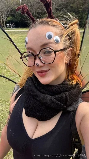 Woman with red hair in a black tank top, wearing insect antennae and wings outdoors.