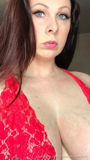 Woman with dark hair and blue eyes wearing red lace top, indoor setting.