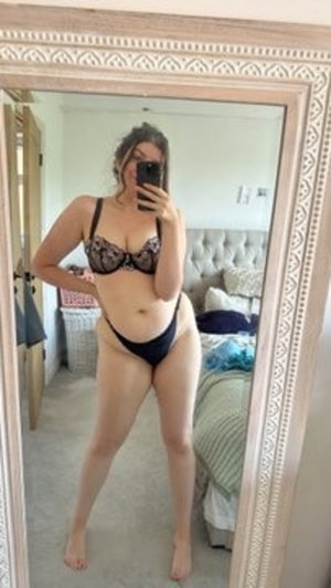 Woman in black lace bra and underwear posing in bedroom mirror selfie.