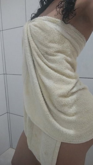 Woman with curly hair wrapped in towel, standing in tiled bathroom.
