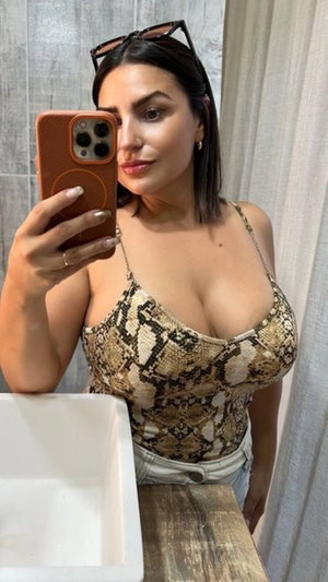 Woman in snake-print top and jeans takes mirror selfie in bathroom.