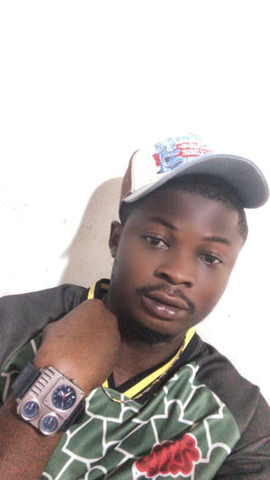 Black man in cap, patterned shirt, watch, indoor selfie.