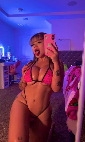 Curvy woman in pink lingerie taking mirror selfie in bedroom.