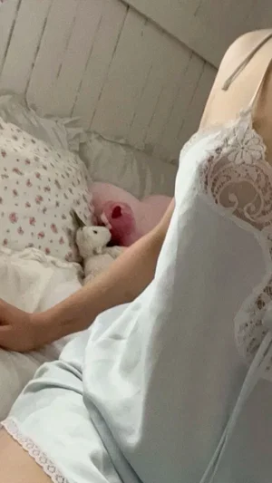 Woman in white lace nightgown lying in bed with stuffed animals, soft lighting.