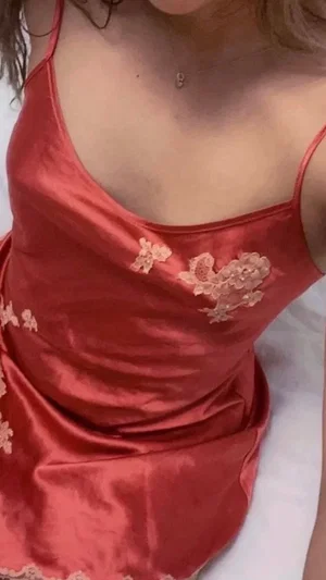 Woman in red satin dress with floral lace details, sitting indoors.