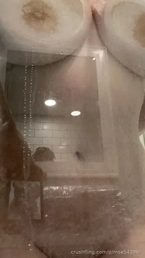 Reflection in mirror shows person in bathroom with tiled walls and shower curtain.
