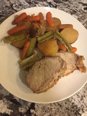 Plate of sliced pork with carrots, potatoes, and celery on a granite countertop.