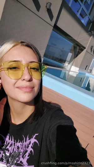 Woman with blonde-tipped hair and yellow sunglasses wearing a black graphic tee, outdoors near a
