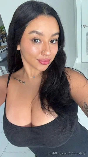 Woman with long black hair in black tank top, indoors, facing camera.
