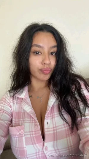 Woman with long dark hair in a pink plaid shirt, posing indoors.