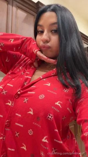 Woman with long black hair in red patterned shirt, posing indoors.
