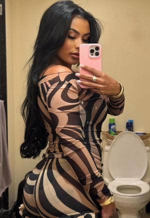 Woman with long black hair in a striped dress takes mirror selfie in bathroom.