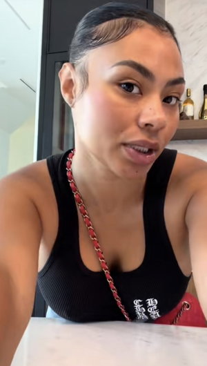 Woman in black tank top with red chain bag, indoors in kitchen setting.