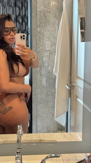 Woman with long dark hair and glasses takes mirror selfie in bathroom wearing brown lingerie,