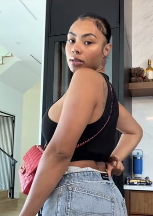 Woman in black crop top and jeans posing indoors, holding pink bag.
