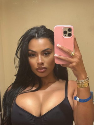 Woman with long black hair in black top taking mirror selfie indoors.