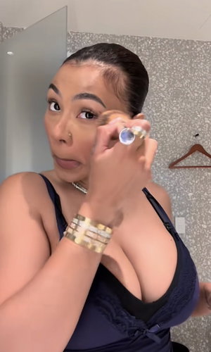 Woman in dark blue lingerie applying makeup in front of mirror, indoors.