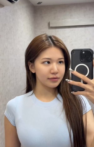 Asian woman with long brown hair in blue t-shirt taking selfie indoors.