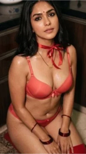Woman in red lingerie posing indoors, sitting on floor with dark hair and bindi.