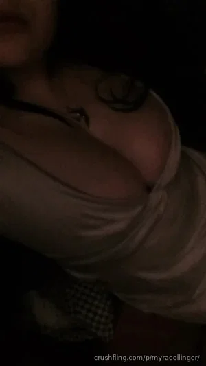 Woman in light-colored top with visible cleavage, dark background, close-up shot.