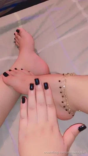 Woman's feet and hand with black nail polish, gold anklet, on patterned surface.