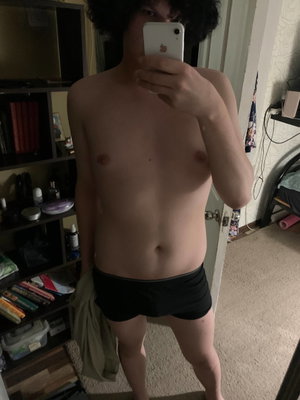Curly-haired man taking mirror selfie in bedroom wearing underwear.