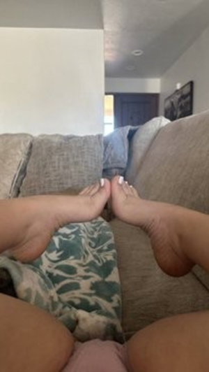 Person sitting on couch, legs spread, feet together, wearing pink bottoms and camo blanket.