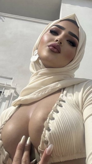 Woman in beige hijab and ribbed top with lace-up front, posing outdoors.
