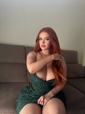 Woman with red hair in green dress sitting on couch, hand on shoulder.