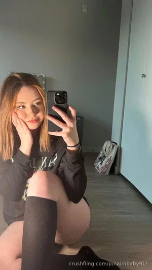 Woman with shoulder-length hair in black long-sleeve top and black thigh-highs, sitting indoors