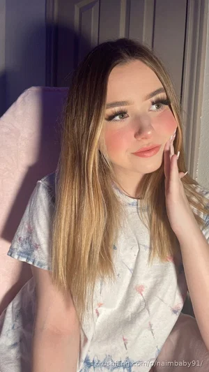 Woman with long blonde hair in a floral t-shirt, sitting indoors with soft lighting.