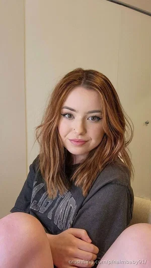 Woman with shoulder-length brown hair wearing a gray t-shirt, sitting indoors with knees up.