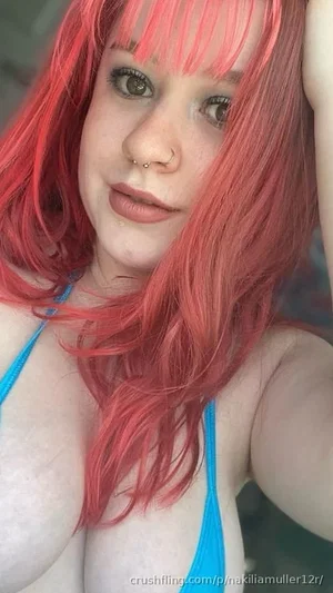 Woman with bright pink hair and blue top, indoors, close-up selfie.