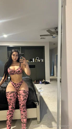 Woman in pink leopard print lingerie and thigh-highs takes mirror selfie in bedroom.