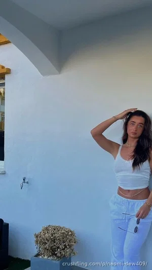 Woman in white crop top and pants posing outdoors near a white wall.