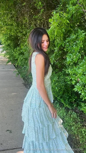 Woman in light green floral dress standing outdoors near green bushes.