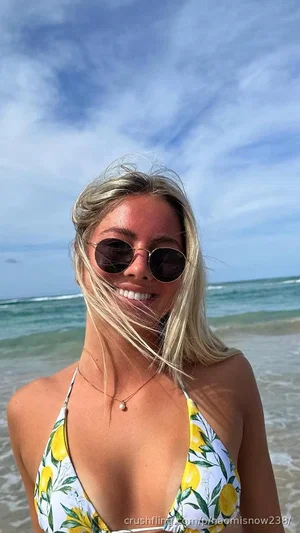 Blonde woman in lemon-print bikini top smiling at beach with ocean behind.