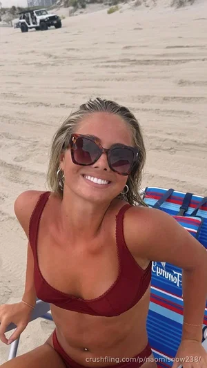 Woman in red bikini smiling on beach, sitting on striped lounge chair.