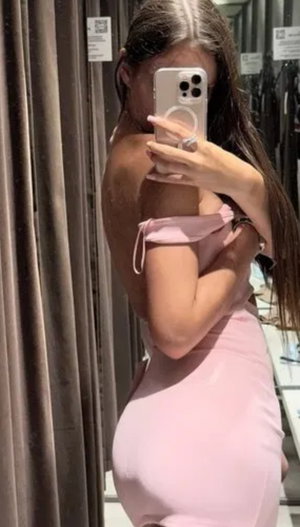 Woman in pink dress taking mirror selfie in fitting room.