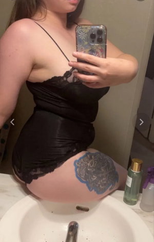 Curvy woman in black lingerie taking bathroom mirror selfie.