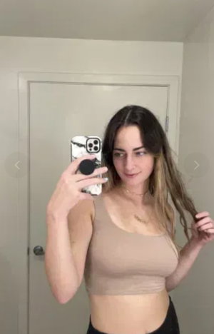 Woman with long brown hair taking mirror selfie in beige crop top indoors.