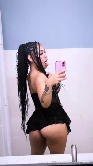 Woman with long braids in black lace outfit taking mirror selfie in bathroom.