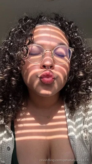 Woman with curly hair and glasses, wearing open shirt, making playful face indoors.