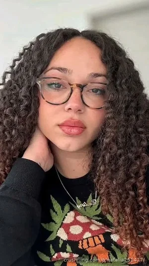 Woman with curly hair and glasses wearing a black sweater with mushroom design, indoors.