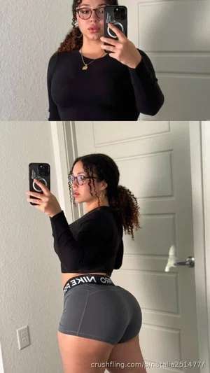 Woman with curly hair in black long-sleeve top and gray shorts taking mirror selfies indoors.