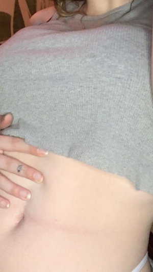 Woman in gray shirt lifting it to show stomach indoors.